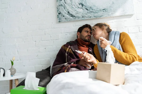 Ill couple holding napkins and nasal spray in bedroom — Stock Photo