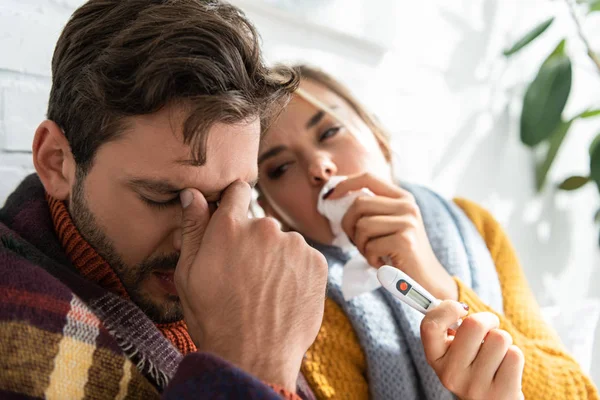 Sick couple with fever holding thermometer and napkins in bed — Stock Photo