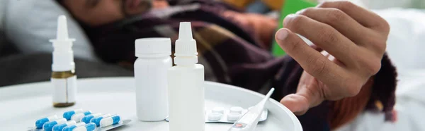 Vista recortada del hombre enfermo acostado en la cama con medicamentos y termómetro en la mesa en casa - foto de stock