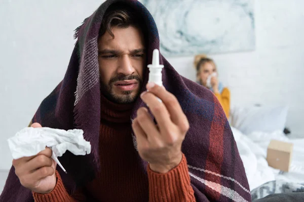 Homme malade tenant pulvérisation nasale et serviette dans la chambre avec femme derrière — Photo de stock