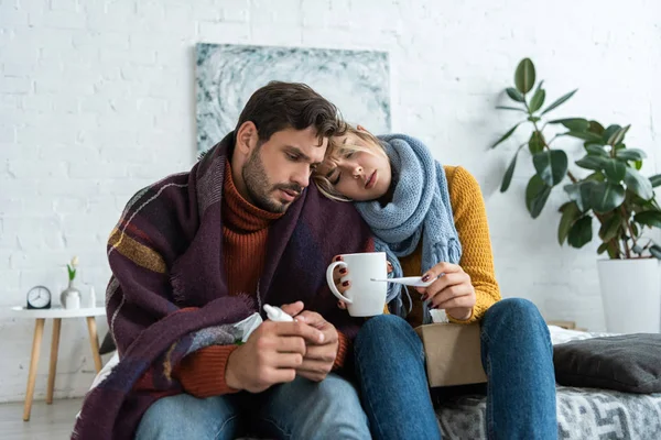 Krankes Paar hält Thermometer, Heißgetränk und Nasenspray im Schlafzimmer — Stockfoto