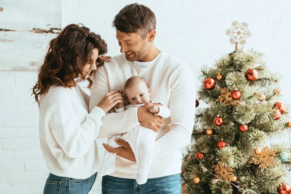 Mujer feliz tocando la mano de adorable bebé sentado en las manos del marido - foto de stock