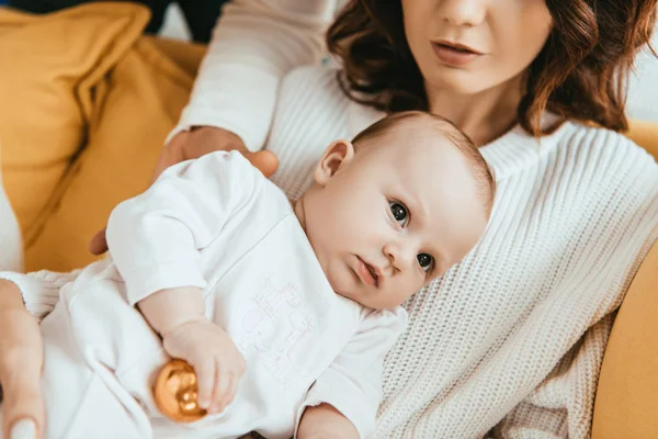 Vista cortada da mulher sentada no sofá com bebê adorável segurando bola de Natal — Fotografia de Stock