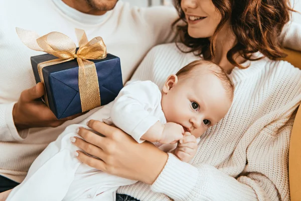 Vue recadrée du mari présentant boîte cadeau à femme heureuse tenant bébé adorable — Photo de stock
