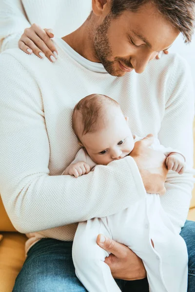 Частичный взгляд женщины, трогающей плечи мужа, держащего очаровательного младенца — стоковое фото