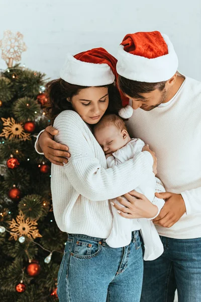 Pai feliz abraçando esposa segurando bebê bonito perto da árvore de Natal — Fotografia de Stock