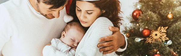 Plan panoramique de père heureux embrassant femme tenant bébé mignon près de l'arbre de Noël — Photo de stock