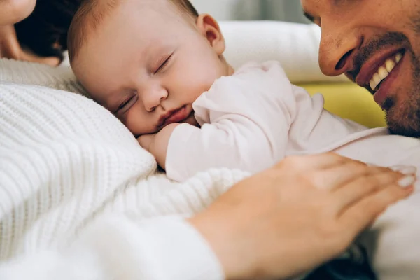 Visão cortada de pai sorridente apoiando-se em bebê adorável deitado em mãos mães — Fotografia de Stock