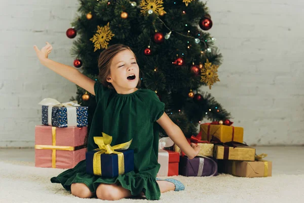 Schläfriges Kind sitzt mit Geschenkbox auf dem Boden, gähnt und dehnt sich mit geschlossenen Augen — Stockfoto