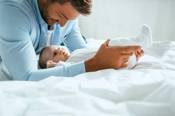 Feliz padre tocando piernas de linda hija pequeña acostada en ropa de cama blanca - foto de stock