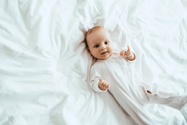 Top view of cute infant in white bodysuit lying on bedding at home — Stock Photo