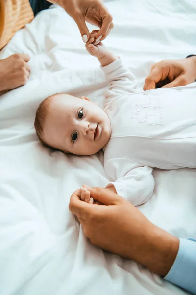 Top view of mother and dad playing with smiling baby lying on white bedding — Stock Photo