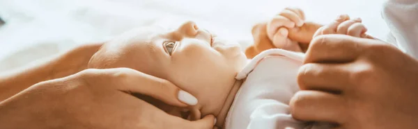 Recortado vista de mamá y papá suavemente tocar bebé acostado en la ropa de cama, tiro panorámico - foto de stock