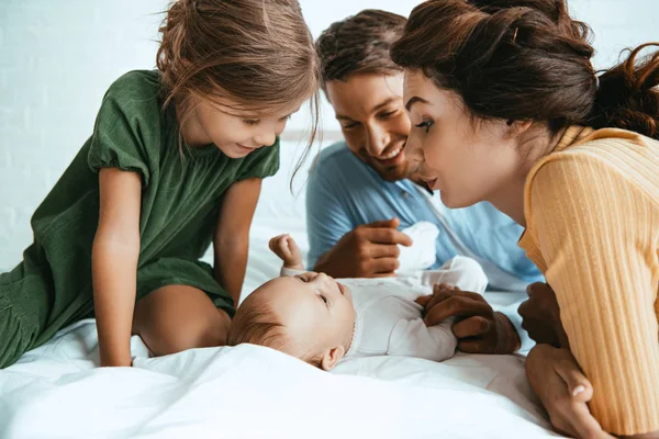 Happy family looking at adorable infant lying on white bedding — Stock Photo