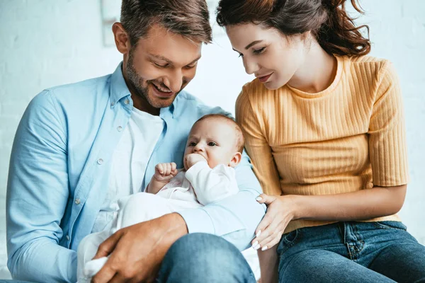 Glückliche Mutter sitzt neben lächelndem Ehemann mit süßer kleiner Tochter — Stockfoto