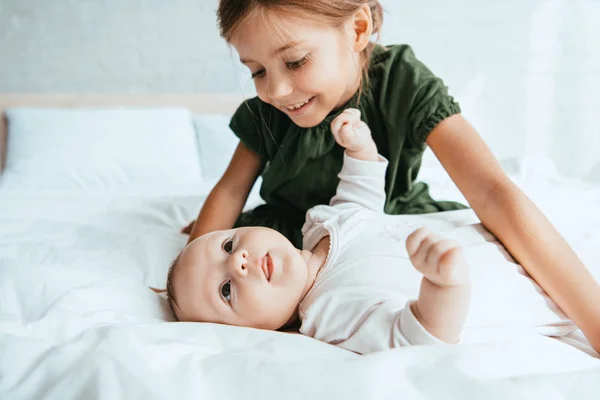 Sonriente niño mirando adorable bebé acostado en blanco ropa de cama - foto de stock