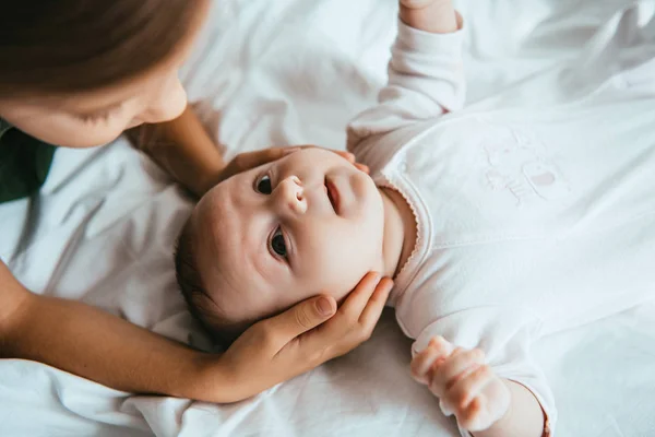 Cropped view of child touching head of adorable baby lying on white bedding — Stock Photo