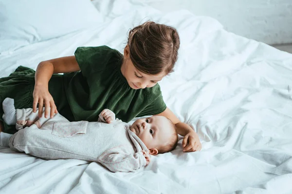 Cute child looking at adorable little sister lying on white bedding — Stock Photo