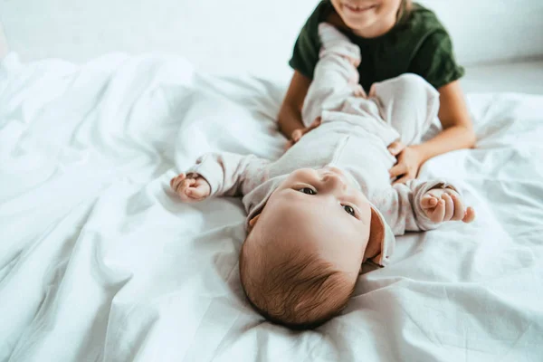 Обрезанный вид улыбающегося ребенка трогающего младенца лежащего на белом постельном белье — стоковое фото