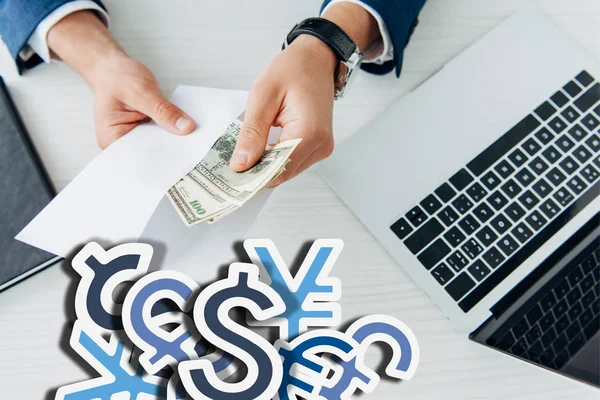 Vista dall'alto dell'uomo d'affari che tiene la busta con le banconote del dollaro vicino al computer portatile sul tavolo con i segni di valuta illustrazione — Foto stock