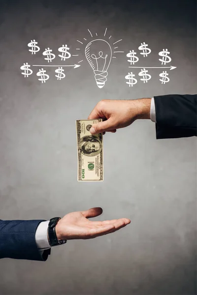 Vue recadrée homme donnant de l'argent à un homme d'affaires sur fond gris avec ampoule et dollar signes illustration — Photo de stock