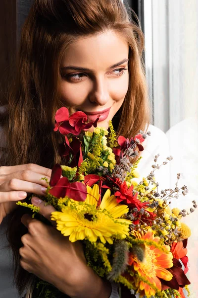 Усміхнена руда жінка з букетом осінніх квітів біля вікна — стокове фото