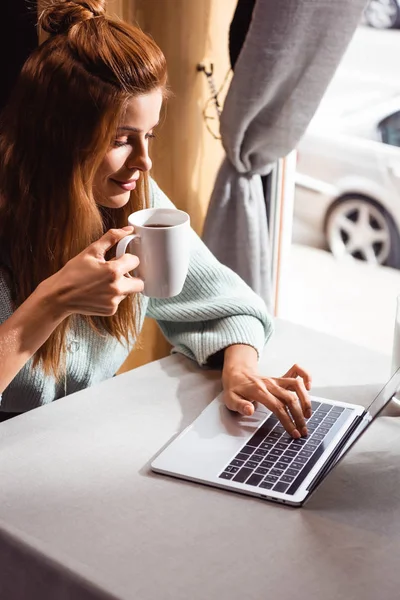 Belle rousse femme avec tasse de café en utilisant un ordinateur portable dans le café — Photo de stock