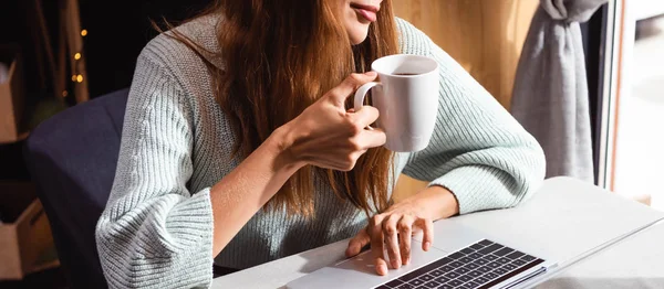 Обрізаний вид жінки, що п'є каву, використовуючи ноутбук у кафе — стокове фото
