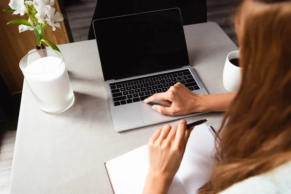 Vista recortada de la mujer que trabaja en el ordenador portátil con pantalla en blanco en la cafetería con taza de café - foto de stock