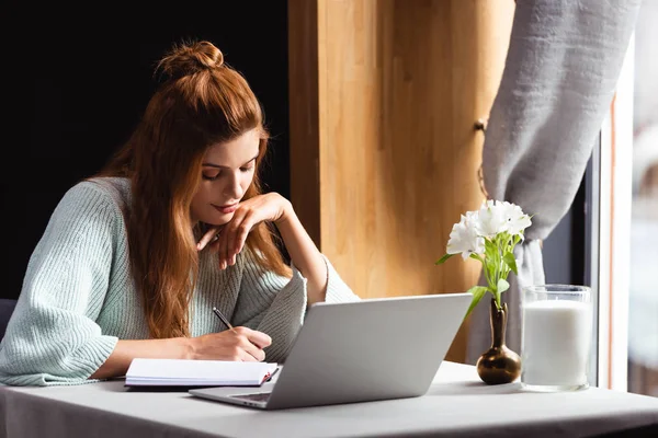 Mulher pensativa escrevendo no bloco de notas e usando laptop no café — Fotografia de Stock