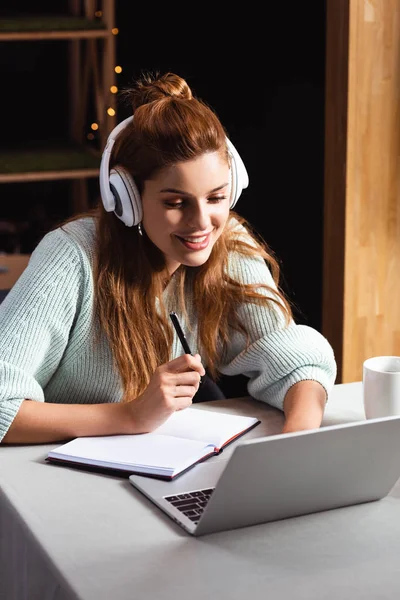 Smiling woman in headphones watching webinar on laptop in cafe — Stock Photo