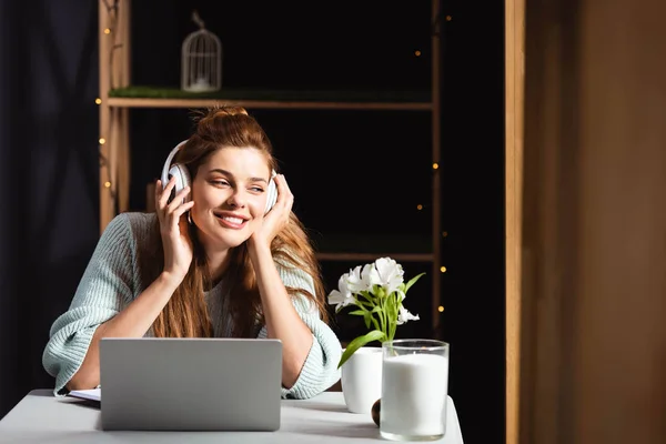 Мечтательная женщина в наушниках смотрит вебинар на ноутбуке в кафе — стоковое фото