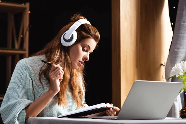 Концентрована жінка в навушниках пише і вивчає онлайн з ноутбуком в кафе — стокове фото
