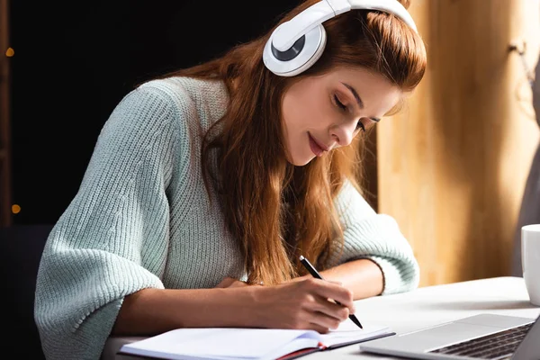 Woman in headphones writing and studying online with laptop in cafe — Stock Photo