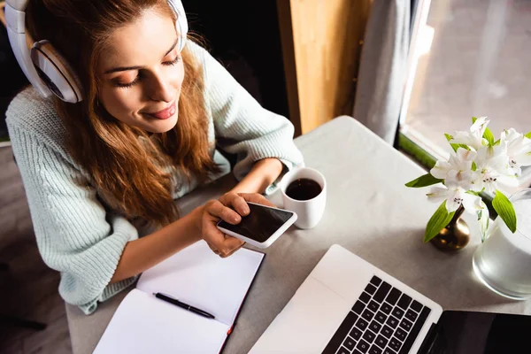 Mujer atractiva en auriculares con teléfono inteligente y portátil en la cafetería - foto de stock