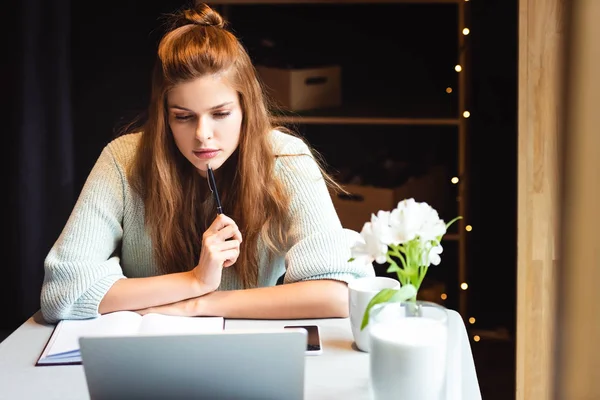 Задумчивая женщина учится онлайн с ноутбуком в кафе — стоковое фото