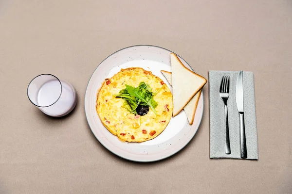 Top view of omelet and toasts in plate with fork and knife and glass of yogurt on table — Stock Photo