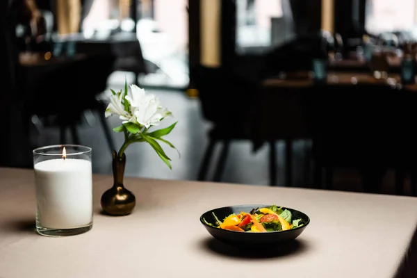 Plato con ensalada en la mesa con vela y flores en la cafetería - foto de stock