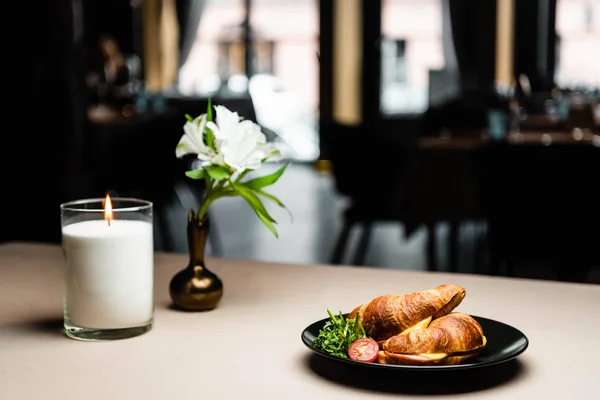 Plato con croissants para el desayuno en la mesa con vela y flores en el restaurante - foto de stock