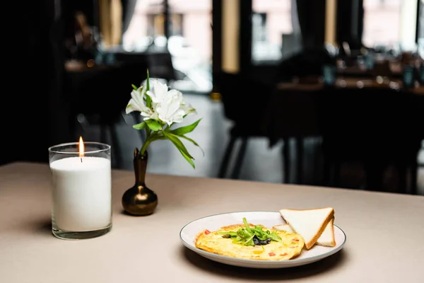 Plate with omelet and toasts for breakfast on table with candle and flowers in cafe — Stock Photo