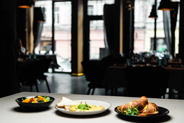 Platos con ensalada, tortilla y croissants para el desayuno en la mesa en el restaurante - foto de stock