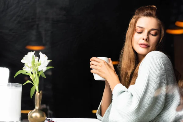 Tierna mujer sosteniendo taza de café en la cafetería con flores - foto de stock