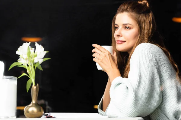 Femme rêveuse tenant tasse de café dans un café avec des fleurs — Photo de stock