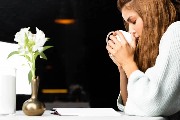 Привлекательная женщина пьет кофе в кафе с цветами — стоковое фото