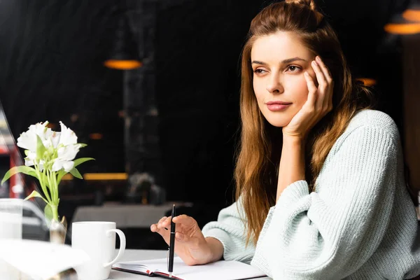 Beautiful pensive woman with notepad and cup of coffee in cafe — Stock Photo