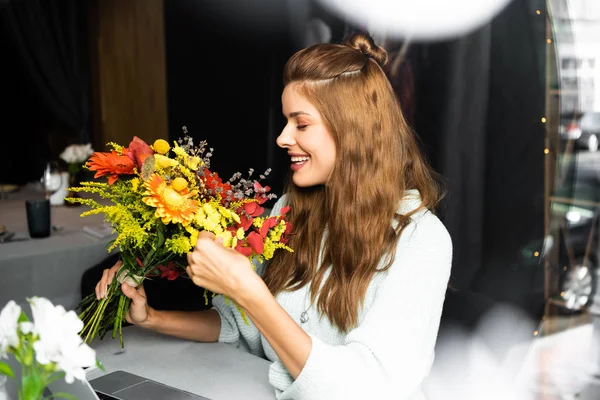 Attraente donna sorridente con mazzo di fiori autunnali in caffè — Foto stock