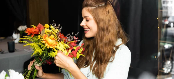 Hermosa mujer pelirroja feliz con ramo de flores de otoño en la cafetería - foto de stock