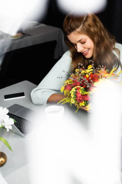 Happy woman with bouquet of autumn flowers in cafe with digital devices — Stock Photo