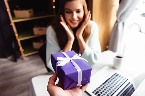 Fuoco selettivo di donna sorpresa che prende il regalo in caffè con computer portatile e tazza di caffè — Foto stock