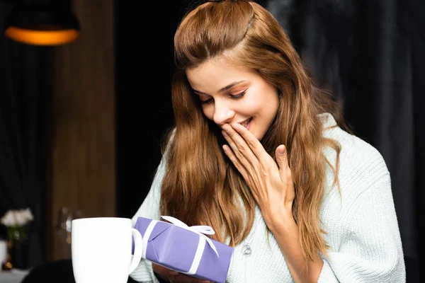 Femme surprise avec boîte cadeau dans un café avec tasse de café — Photo de stock